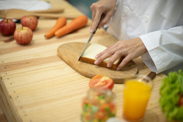 Chef professionally cuts bread on a chopping board in a kitchen full of cooking ingredients.