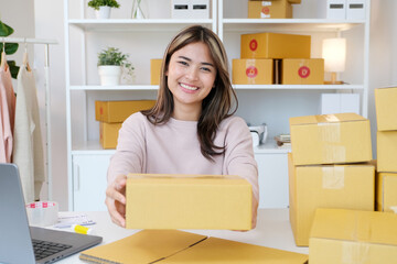 Young asian small business owner holding prodect boxes while smiling and looking at camera, online shopping