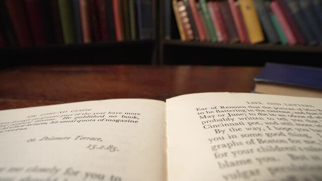 Macro reverse dolly across page in book in library as hand turns the page