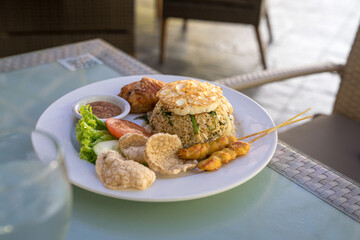 Fried rice served with fried chicken, fried egg and satay. Asian style.