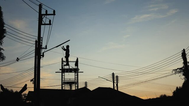 Electrician changing the street light on the electric pole. Silhouette of a worker on scaffolding sunset sky.