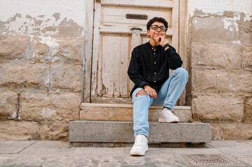 Young transgender man posing sitting on the front steps of a house.
