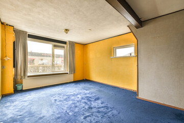 an empty room with yellow walls and blue carpeted floor in front of the window looking out onto the street