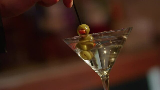 Stirring olive martini into cocktail glass slowmo