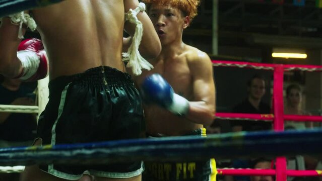 4K Cinematic slow motion footage of two young Thai men fighters on a boxing ring having a Muay Thai boxing fight in a stadium in Chiang Mai, Thailand