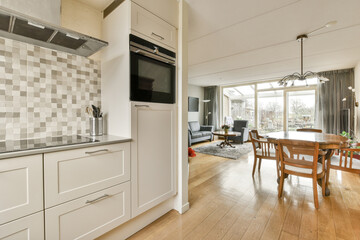 a kitchen and dining area in a house with white cabinets, wood flooring and an open door leading to the patio