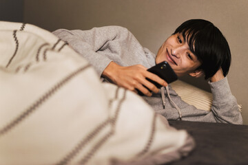 夜に暗い寝室でベッドに寝ながらスマートフォンを操作する30代の男性