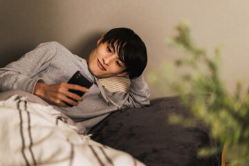 寝室で布団に包まりながらスマートフォンを操作する30代の男性