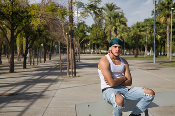 Fototapeta na wymiar Latino and Hispanic boy, young, rebellious, with headscarf, arms crossed and looking defiantly at camera, sitting on a bench. Troubled concept, rebel, gangs, defiant.