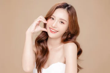 Fotobehang Young Asian beauty woman curly long hair with korean makeup style touch her face and perfect skin on isolated beige background. Facial treatment, Cosmetology, plastic surgery. © Auttapol