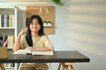 Cute teenager girl with a lovely engaging smile sitting at a desk in living room. Homeschooling, learning, self education 