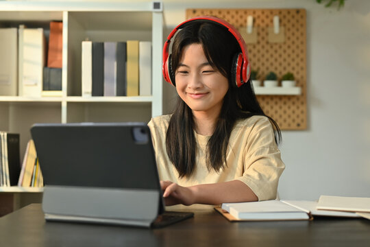 Happy asian girl wearing headphones sitting at table learning online at virtual class on laptop. Distance education concept