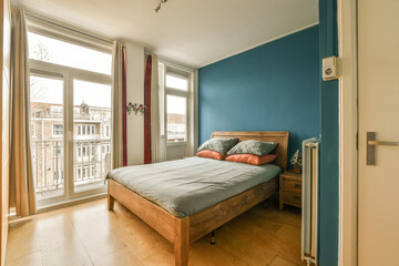 a bedroom with blue walls and wood flooring in the room, there is an open door leading to another...