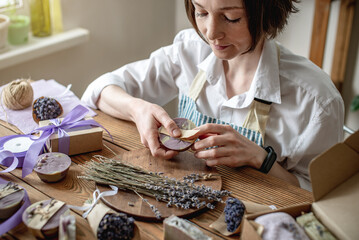 Woman in an apron is packing natural lavender soap and decorating it with lavender flowers. Concept...