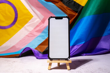 Mobile phone with white screen for copy space on Rainbow LGBTQIA flag made from silk material...