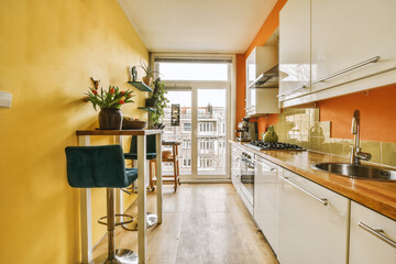 a kitchen with orange walls and wood flooring in the center of the photo is an open door leading to a balcony