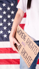 Woman is holding a sign Womens Rights Are Human Rights US flag on background. Protest against anti...