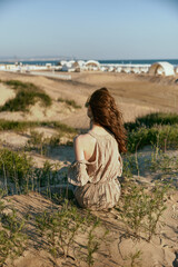 a woman sits with her back to the camera on the sea coast enjoying the sea view