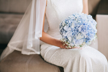The bride in a white dress holds a delicate wedding bouquet in her hands.
