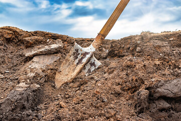Dirty shovel in fresh soil at a construction site in a pit. Deep hole in the ground. Earthworks, manual refinement of the soil. Dig deep ditches and holes. - obrazy, fototapety, plakaty