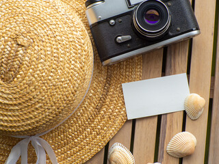 Wooden background with straw hat, photo camera, shells and space for text. Card design with copy...