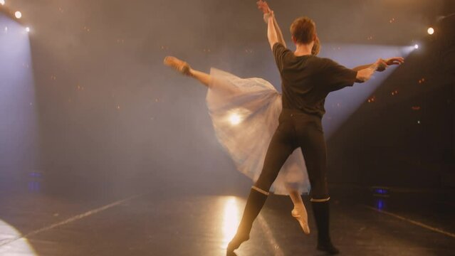 Ballet dancers practice ballet movements and rehearse choreography on classic theater stage illuminated by spotlight. Man and woman prepare theatrical dance performance. Art of classical ballet dance.