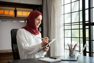 Young Arabic female entrepreneur wearing a hijab working online with a laptop at office.