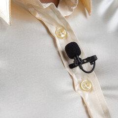 The lavalier microphone is secured with a clip on a women shirt close-up. Audio recording of the sound of the voice on a condenser microphone