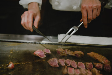 Close-up of a chef's hand in motion  holding a knife and fork to cut steak on a teppanyaki stove in Kobe stake restaurant.