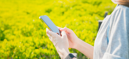 Woman standing on a bridge in the garden and using smartphone in public areas, During leisure time. The concept of using the phone is essential in everyday life.