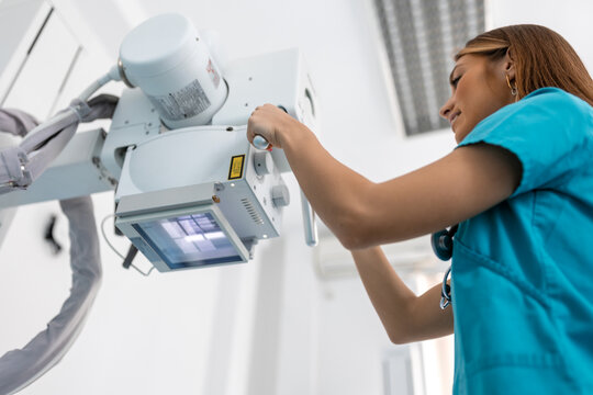 Doctor looking at X-ray machine in clinic. Female doctor sets up the machine to x-ray over patient. Radiologist and patient in a x-ray room. - Powered by Adobe