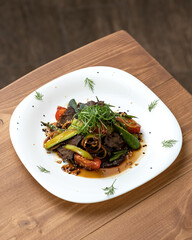 Thai salad with beef, vegetables, noodles and teriyaki sauce. Dish is decorated with sesame seeds and dill on white plate. Asian cuisine. Wooden table. View from above. Copy space.
