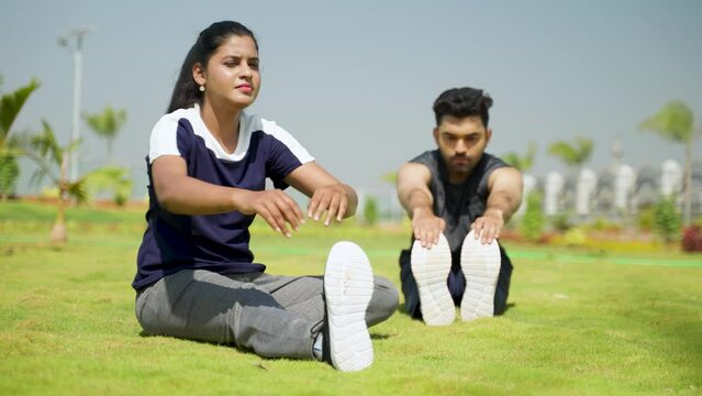 serious Young Indian people doing stretching exercise by touching feet vy sitting on park - concept of fitness training, active lifestyle and morning routine