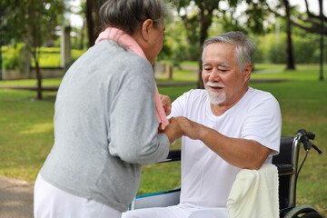 Fototapeta premium Asian senior woman or caregiver helping and consoling senior man walk with wheelchair at park outdoor. Elderly wife taking good help care and support of elder husband patient outside the house.