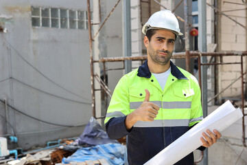 Caucasian technician civil engineer man or specialist inspector standing and planing real estate project work with blueprint while showing thumb up at Industrial building site. Construction concept