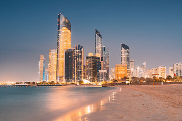 Stunning sandy beach near Corniche seaside embankment with great night view of Abu Dhabi, UAE towering skyscrapers