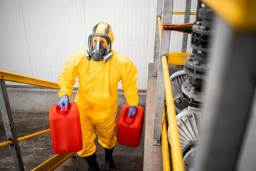 Fototapeta premium Fully protected worker in hazmat suit and gas mask carrying chemicals. Industrial interior.
