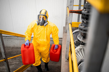 Fully protected worker in hazmat suit and gas mask carrying chemicals. Industrial interior.