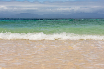 Soft wave on the beach with yellow sand against the backdrop of mountains and the sea