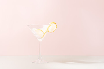Glass goblet with ice and lime slices against pink background.