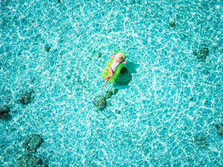 Aerial view of an attractive woman taking a relaxing sunbath on a pinapple shaped float over the turquoise waters of the Maldives
