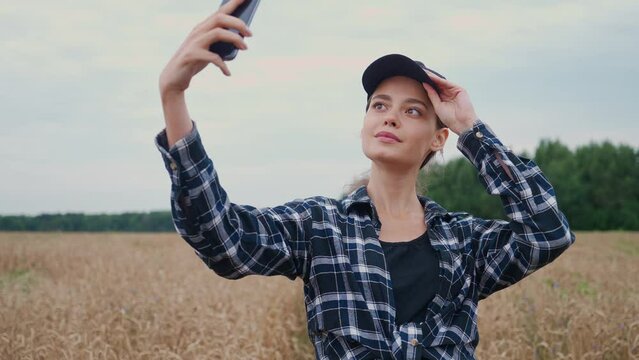 Countryside, pretty woman farmer standing in a field of rye and takes selfie pictures on a smartphone, investigating plants.