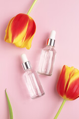 Obraz na płótnie Canvas Cosmetic bottles made of amber glass and tulips on a pink background. Concept of natural organic cosmetics. Herbal homeopathic products