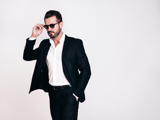 Portrait of handsome confident stylish hipster lambersexual model. Sexy modern man dressed in black elegant suit. Fashion male posing in studio, isolated on white. Sunglasses