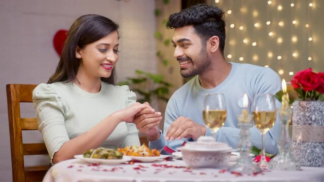 Happy Indian young man putting or placing engagement ring to girlfriend during candle light dinner - concept of valentines day accepted , marriage proposal and romantic night
