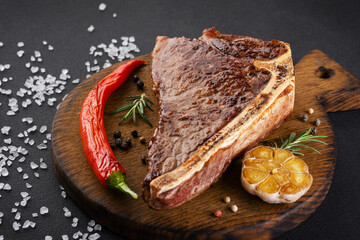 Grilled new york steak on wooden board background with salt, pepper, rosemary, garlic and chili.