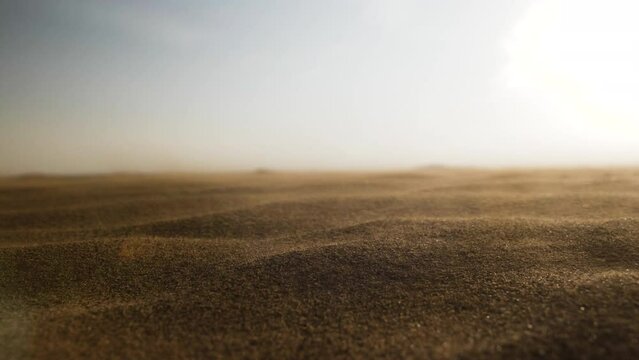 Sunset, sun shining over sand blowing in slow motion in the wind in slow motion in middle eastern desert landscape near Dubai in the United Arab Emirates.