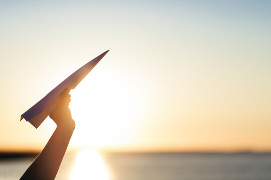 Silhouette Of A Person's Hand Holding Paper Airplane Against Sunrise