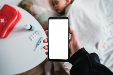 Mother standing near sick child holding smartphone calling doctor pediatrician