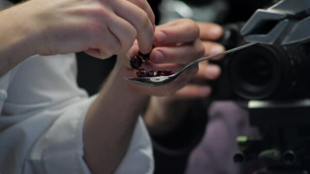 static macro shot of cook carefully arranging cherries in spoon for filming, camera on background